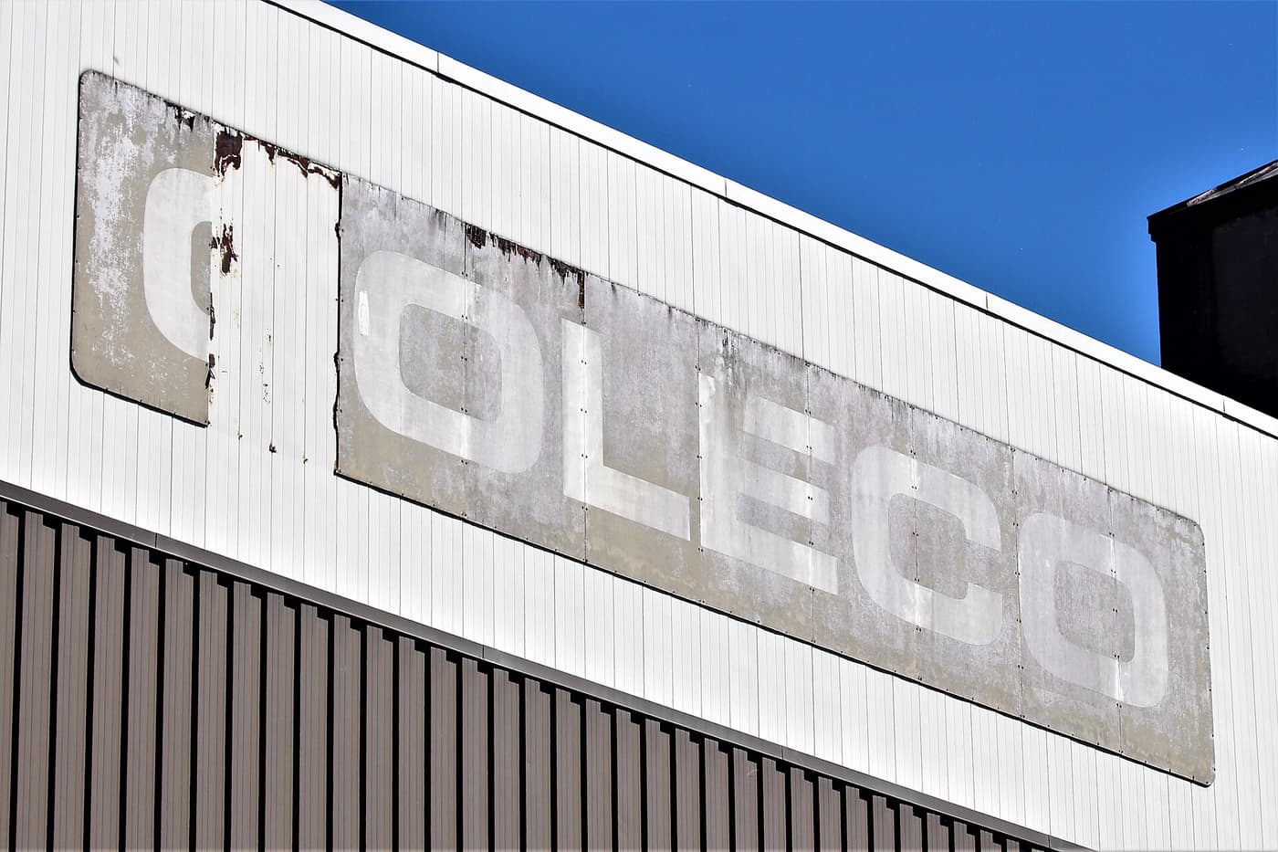 A faded COLECO sign on a white industrial building