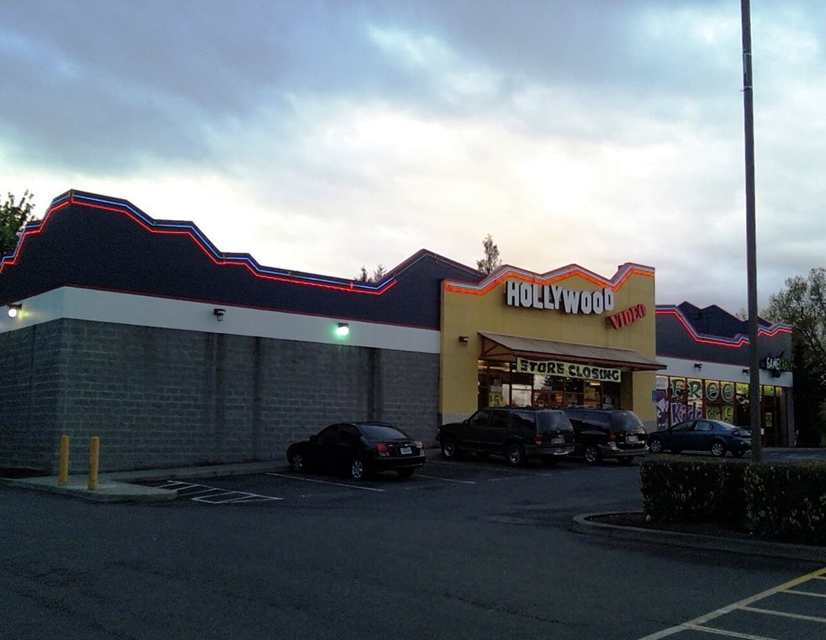 Hollywood Video store at dusk with red and blue neon along the roofline and a Store Closing banner over the entrance