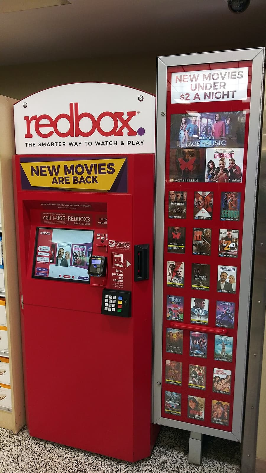 A red Redbox kiosk with a touch screen standing inside a supermarket entrance