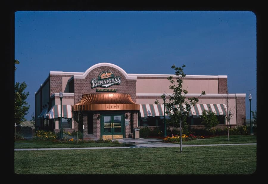 A Bennigan’s restaurant with green awnings and a pitched roof beside a parking lot